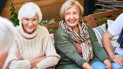 Pretty senior women with charming smiles listening to their male friend with interest while having gathering at cozy small patio